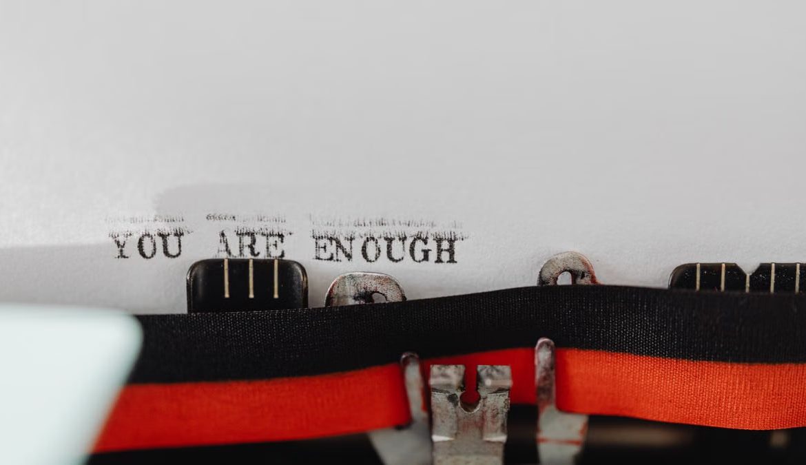 Close-up of a typewriter with the message 'YOU ARE ENOUGH' typed on paper.